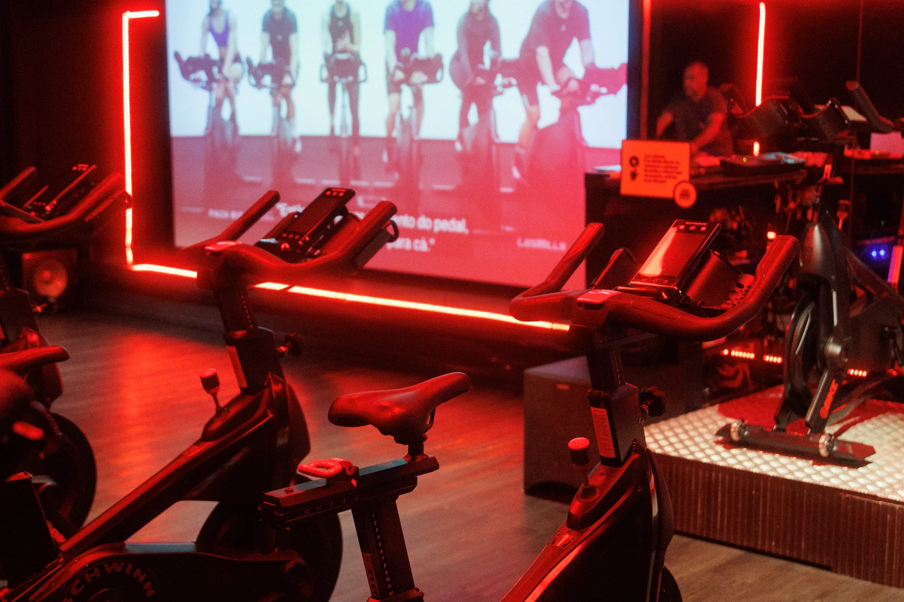 Sala atual de ciclismo indoor da The Best, com bicicletas, projeção e iluminação vermelha